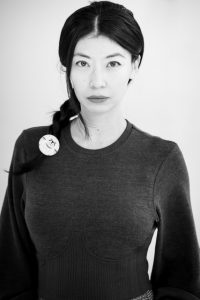 Mila Zuo studio portrait wearing a dark crew-neck top and cartoon bear hair fastener