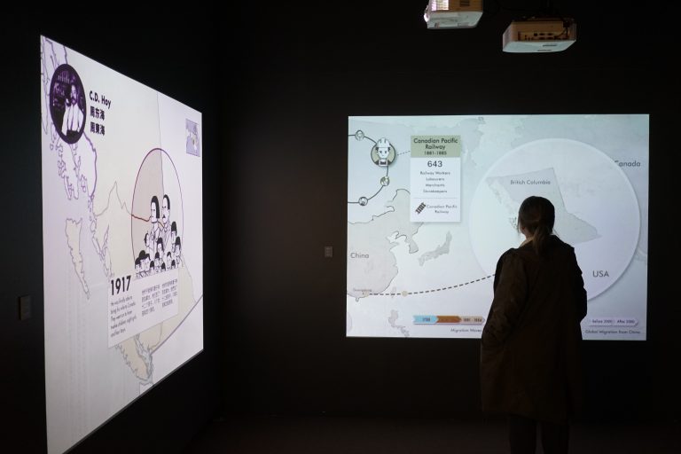 A silhouette stands in front of a projection display at the "A Seat at the Table" MOV exhibit, showing the migration path of workers between China and BC in the early 20th century.
