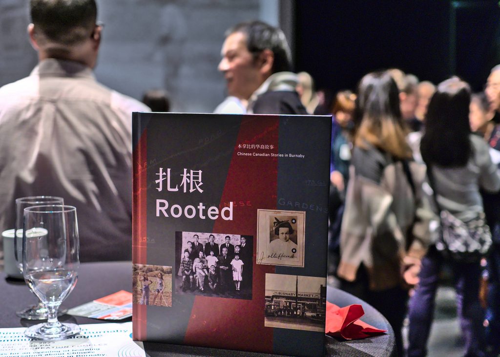 A physical copy of Rooted being propped up on a table during the book launch event, with people conversing with each other in the background.